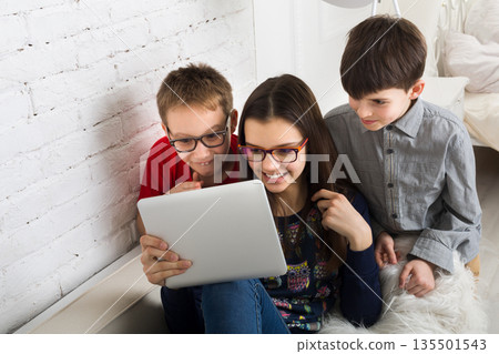 Group of kids in eye glasses look into tablet. Children computer games, social networks and media addiction concept. Girl and boys with gadget. Communication technologies. 135501543