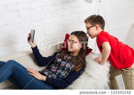 Children in eye glasses look into tablet. Computer games, social networks and media addiction concept. Girl and boy with tablet. Eyesight, eyewear for kids. 135501548