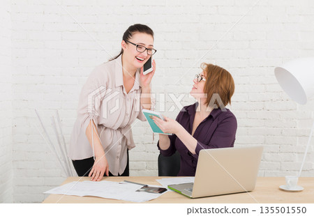 Two happy women in the office. Teamwork, business communication. Middle-aged architects designers in team work discuss project. Start up discussion. Female coworkers. 135501550