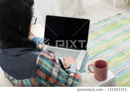 Freelancer woman works at home, back view, mockup. Home office, freelance. Unrecognizable brunette girl with laptop with blank screen with coffee cup, copy space 135501551