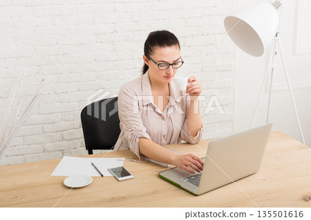 Middle-aged business woman in office with coffee. Female using laptop computer at workplace, copy space. Coffee-break, rest concept 135501616