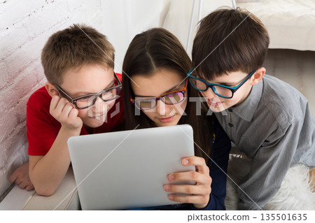 Children computer games, social networks and media addiction concept. Group of kids in eye glasses look into tablet. Girl and boys with tablet. 135501635