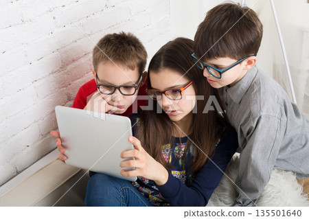 Group of kids in eye glasses look into tablet. Children computer games, social networks and media addiction concept. Girl and boys with tablet. Communication technologies. 135501640