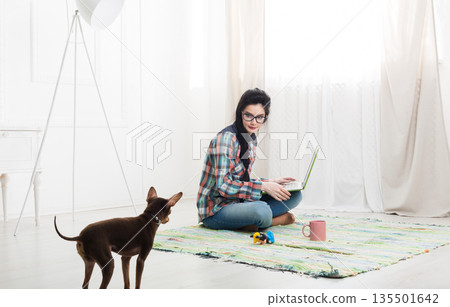 Young girl in computer glasses on carpet with laptop and dog chihuahua. Hipster freelancer woman works at home. Home office, freelance. 135501642