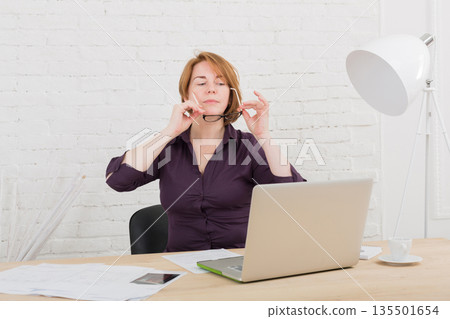 Middle-aged Woman in the office. Female architect using laptop computer and smartphone. Office worker. Redhead caucasian woman in protective glasses with computer. High-key, soft tone. 135501654