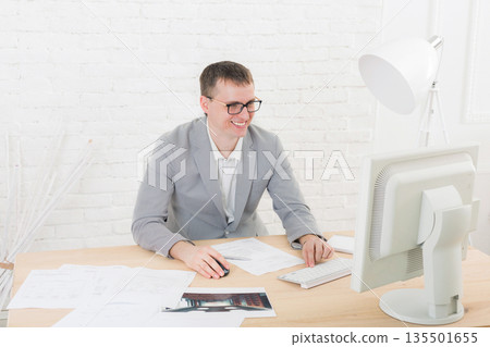 Young businessman working with laptop in modern white office interior. Handsome man in suit, successful employee at work with computer. Lifestyle portrait Young businessman working with laptop in modern white office interior. Handsome man in suit, successful employee at work with computer. Lifestyle portrait 135501655