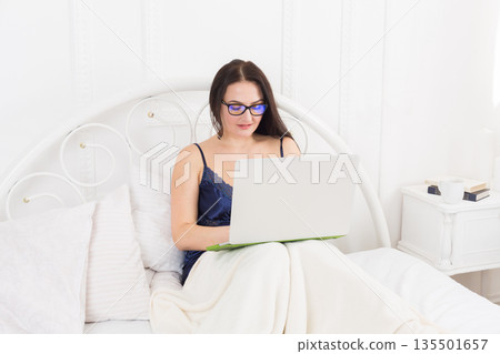 Sunday morning in bed. Middle aged woman surfing internet at her laptop computer. High key. Sunday morning in bed. Middle aged woman surfing internet at her laptop computer. High key. 135501657