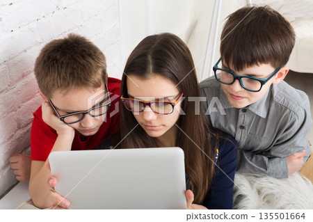 Group of kids in eye glasses look into tablet. Children computer games, social networks and media addiction concept. Girl and boys with tablet. Communication technologies. 135501664
