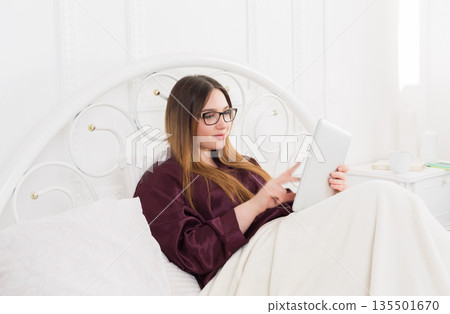 Sunday morning in bed. Young woman in surfing internet at her tablet pc, copy space Sunday morning in bed. Young woman in surfing internet at her tablet pc, copy space 135501670