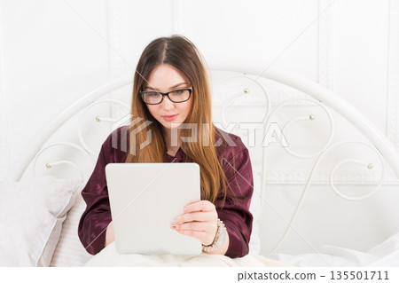 Sunday morning in bed. Young woman in surfing internet at her tablet pc, copy space Sunday morning in bed. Young woman in surfing internet at her tablet pc, copy space 135501711