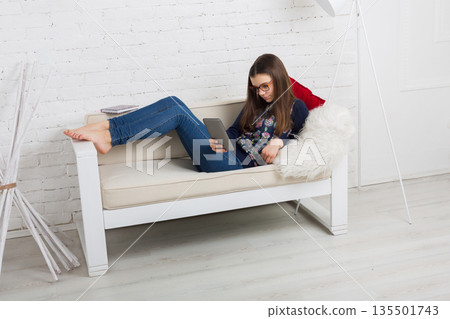 Teenage girl in eye glasses look into tablet, lying on sofa. Children computer games, social networks and media addiction concept. Communication technologies, copy space 135501743