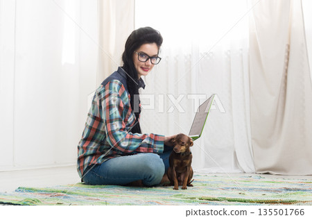 Young girl in computer glasses on carpet with laptop and dog chihuahua. Hipster freelancer woman works at home. Home office, freelance. 135501766