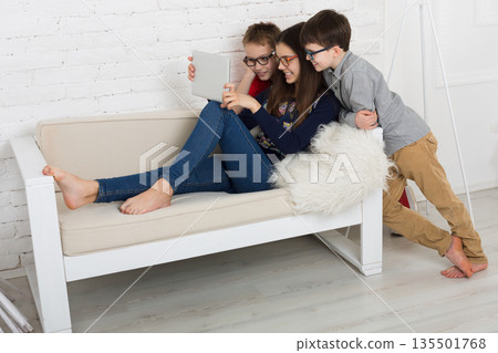 Children computer games, social networks and media addiction concept. Group of kids in eye glasses look into tablet. Girl and boys with device 135501768