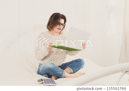 Young woman freelancer works at home in bed with laptop. Engrossed Girl in eyeglasses. Freelance. Young woman freelancer works at home in bed with laptop. Engrossed Girl in eyeglasses. Freelance. 135501769
