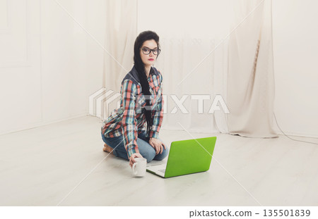 Freelancer woman working on floor, copy space. Home office, freelance. Brunette girl with laptop in modern interior. Freelancer woman working on floor, copy space. Home office, freelance. Brunette girl with laptop in modern interior. 135501839