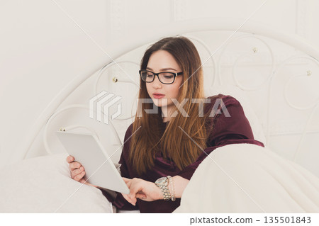Sunday morning in bed. Young woman in surfing internet at her tablet pc, copy space Sunday morning in bed. Young woman in surfing internet at her tablet pc, copy space 135501843