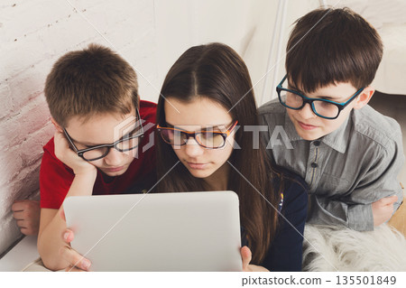 Group of kids in eye glasses look into tablet. Children computer games, social networks and media addiction concept. Girl and boys with gadget. Communication technologies. 135501849