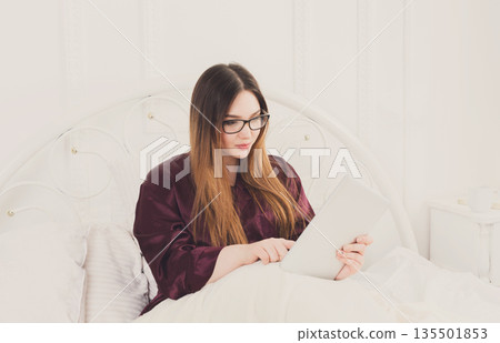 Sunday morning in bed. Young woman in surfing internet at her tablet pc, copy space Sunday morning in bed. Young woman in surfing internet at her tablet pc, copy space 135501853