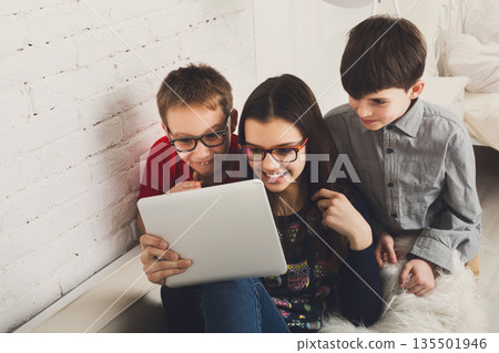 Group of kids in eye glasses look into tablet. Children computer games, social networks and media addiction concept. Girl and boys with gadget. Communication technologies. 135501946