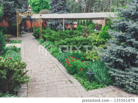 Beautiful landscape design, garden path to gazebo, evergreen bushes and shrubs in sunlight. Modern landscaping. Summer garden or park design. Beautiful landscape design, garden path to gazebo, evergreen bushes and shrubs in sunlight. Modern landscaping. Summer garden or park design. 135501979