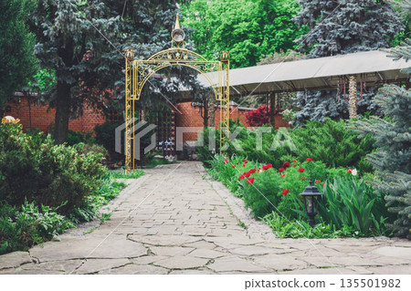 Beautiful landscape design, garden path to gazebo, evergreen bushes and shrubs in sunlight. Modern landscaping. Summer garden or park design. Beautiful landscape design, garden path to gazebo, evergreen bushes and shrubs in sunlight. Modern landscaping. Summer garden or park design. 135501982
