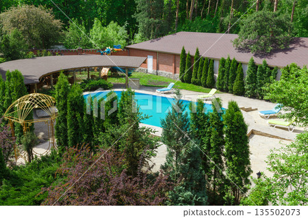 Luxury swimming pool beside the modern hotel and spa resort. Landscape design of resort territory. Beautiful trees and bushes. Luxury swimming pool beside the modern hotel and spa resort. Landscape design of resort territory. Beautiful trees and bushes. 135502073