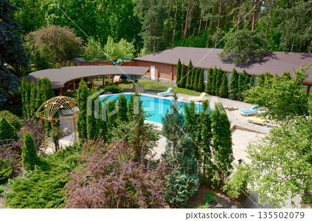 Luxury swimming pool beside the modern hotel and spa resort. Landscape design of resort territory. Beautiful trees and bushes. Luxury swimming pool beside the modern hotel and spa resort. Landscape design of resort territory. Beautiful trees and bushes. 135502079
