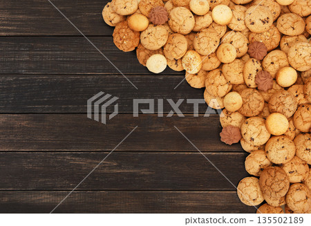 Cookies background. Sweet chocolate chips biscuits heap at brown rustic wood background with copy space. Oatmeal, chocolated drops and other sweets. Fattening dessert for tea on wooden table top view 135502189