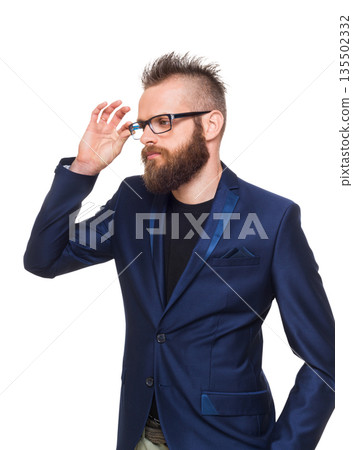 Young bearded man isolated at white background. Portrait of a confident stylish guy in eyeglasses looking at camera. Boy style, trendy hipster with cool hairstyle in blue suit. 135502332