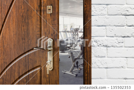 Opened door to modern gym interior with equipment. Entrance to fitness club with row of exercise stationery bikes for fitness cardio training. Welcome to sport, healthy lifestyle concept Opened door to modern gym interior with equipment. Entrance to fitness club with row of exercise stationery bikes for fitness cardio training. Welcome to sport, healthy lifestyle concept 135502353