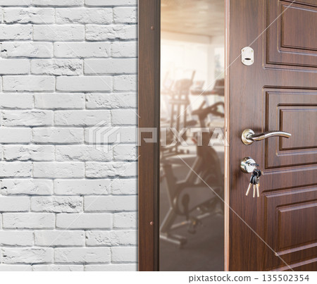 Opened door to modern gym interior with equipment. Entrance to fitness club with row of exercise stationery bikes for fitness cardio training. Welcome to sport, healthy lifestyle concept 135502354