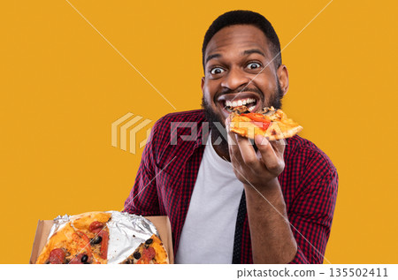 Portrait Of Funny Black Guy Eating Pizza Slice Smiling To Camera Overeating Posing In Studio Over Yellow Background. Male Foodie Enjoying Junk Food. Unhealthy Nutrition And Cheat Meal Concept Portrait Of Funny Black Guy Eating Pizza Slice Smiling To Camera Overeating Posing In Studio Over Yellow Background. Male Foodie Enjoying Junk Food. Unhealthy Nutrition And Cheat Meal Concept 135502411