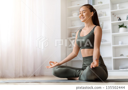 Beautiful young asian woman smiling gently while practicing yoga at home, calm korean female meditating on mat in living room, performing mudra, embodying relaxation and joy, copy space Beautiful young asian woman smiling gently while practicing yoga at home, calm korean female meditating on mat in living room, performing mudra, embodying relaxation and joy, copy space 135502444