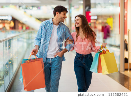 Successful Shopping. Couple Carrying Shopper Bags Walking Holding Hands In Modern Hypermarket Indoor. Buyers Buying New Clothes During Great Seasonal Sales On Weekend. Shopaholism And Commerce Successful Shopping. Couple Carrying Shopper Bags Walking Holding Hands In Modern Hypermarket Indoor. Buyers Buying New Clothes During Great Seasonal Sales On Weekend. Shopaholism And Commerce 135502451