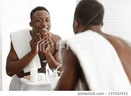 Happy Black Man Touching Smooth Face Skin After Shaving Standing Near Mirror In Bathroom At Home. Male Facial Skincare, Morning Beauty Routine And Self-Care Cosmetics Concept Happy Black Man Touching Smooth Face Skin After Shaving Standing Near Mirror In Bathroom At Home. Male Facial Skincare, Morning Beauty Routine And Self-Care Cosmetics Concept 135502452