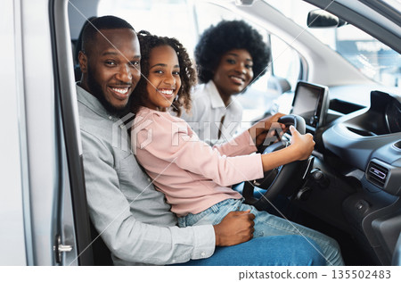 Happy Afro family sitting in new car, going on test drive, buying automobile in dealership store. Black customers checking vehicle before purchase or rental, posing inside car salon, smiling at camera Happy Afro family sitting in new car, going on test drive, buying automobile in dealership store. Black customers checking vehicle before purchase or rental, posing inside car salon, smiling at camera 135502483