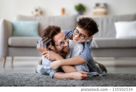 Father son bonding. Daddy lying on carpet carrying boy on back and smiling, having fun at home on weekend, spending time together. Parents and children being friends, single dad concept Father son bonding. Daddy lying on carpet carrying boy on back and smiling, having fun at home on weekend, spending time together. Parents and children being friends, single dad concept 135502534