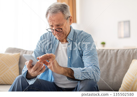 Poor Eyesight In Older Age, Macular Degeneration Concept. Confused Mature Male In Eyeglasses Squinting Eyes Reading Message On Cell Phone Having Ophtalmic Issue Problems With Vision Sitting On Sofa Poor Eyesight In Older Age, Macular Degeneration Concept. Confused Mature Male In Eyeglasses Squinting Eyes Reading Message On Cell Phone Having Ophtalmic Issue Problems With Vision Sitting On Sofa 135502580
