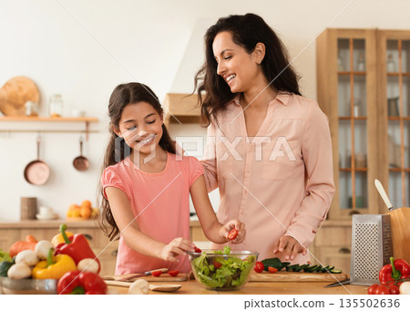 Joyful Middle Eastern Mother And Preteen Daughter Cooking Healthy Vegetable Salad For Dinner At Modern Kitchen Interior. Mom And Kid Girl Cutting Veggies Preparing Food Together. Family Nutrition Joyful Middle Eastern Mother And Preteen Daughter Cooking Healthy Vegetable Salad For Dinner At Modern Kitchen Interior. Mom And Kid Girl Cutting Veggies Preparing Food Together. Family Nutrition 135502636