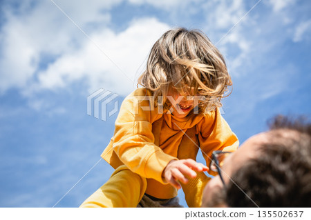 low angle view on smiling child in yellow clothes watching father low angle view on smiling child in yellow clothes watching father 135502637