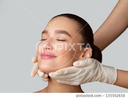 Beauty Treatment. Calm girl receiving face massage from cosmetologist who wearing protective gloves, isolated Beauty Treatment. Calm girl receiving face massage from cosmetologist who wearing protective gloves, isolated 135502638