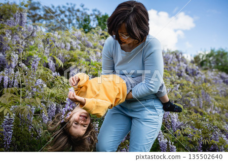Mother in blu and laughing daughter in yellow clothes playing outside Mother in blu and laughing daughter in yellow clothes playing outside 135502640