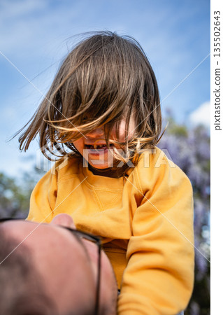 low angle view of happy child in yellow top looking at dad hold in his hands low angle view of happy child in yellow top looking at dad hold in his hands 135502643
