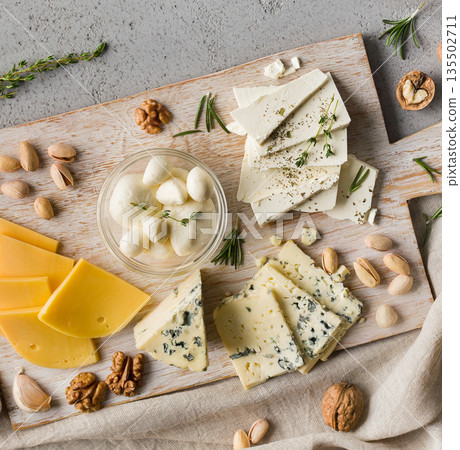Assortment of cheese with nuts and rosmary on wooden board over grey concrete background, top view. 135502711
