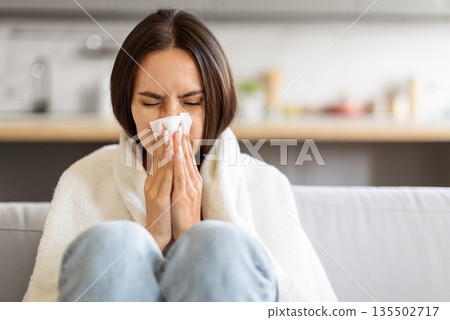 Sick Young Woman Blowing Nose In Paper Tissue While Sitting On Couch At Home Covered In Blanket, Portrait Of Ill Caucasian Lady Suffering Runny Nose, Feeling Unwell, Having Seasonal Flu, Copy Space Sick Young Woman Blowing Nose In Paper Tissue While Sitting On Couch At Home Covered In Blanket, Portrait Of Ill Caucasian Lady Suffering Runny Nose, Feeling Unwell, Having Seasonal Flu, Copy Space 135502717