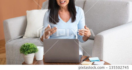 Online Briefing And Virtual Conference. Portrait of confident middle-aged woman sitting on the sofa, using laptop computer on desk, having video call, talking to webcam, explaining and discussing Online Briefing And Virtual Conference. Portrait of confident middle-aged woman sitting on the sofa, using laptop computer on desk, having video call, talking to webcam, explaining and discussing 135502745