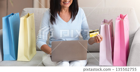 Buying Gifts And Presents Concept. Happy Adult Lady Using Laptop, Holding Credit Card, Ordering Goods In Internet Store, Sitting At Home With Shopping Bags On The Couch, Copy Space Buying Gifts And Presents Concept. Happy Adult Lady Using Laptop, Holding Credit Card, Ordering Goods In Internet Store, Sitting At Home With Shopping Bags On The Couch, Copy Space 135502755