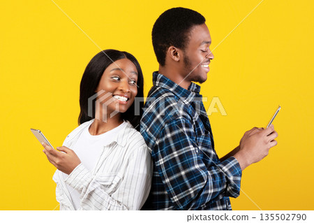 Blogs, social media, unusual message and interesting event. Cheerful young african american lady look over shoulder in smartphone of smiling husband, isolated on yellow background, studio shot 135502790