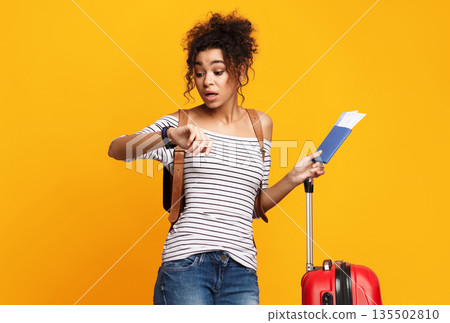 Black Traveler Girl Being Late For Flight Checking Time Standing With Suitcase And Tickets Over Yellow Background. Studio Shot Black Traveler Girl Being Late For Flight Checking Time Standing With Suitcase And Tickets Over Yellow Background. Studio Shot 135502810
