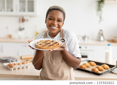 Cheerful happy funny millennial african american female cook in apron showing fresh pie in white kitchen interior. Pretty housewife cooking at home homemade eat, health care and food blog at home Cheerful happy funny millennial african american female cook in apron showing fresh pie in white kitchen interior. Pretty housewife cooking at home homemade eat, health care and food blog at home 135502822